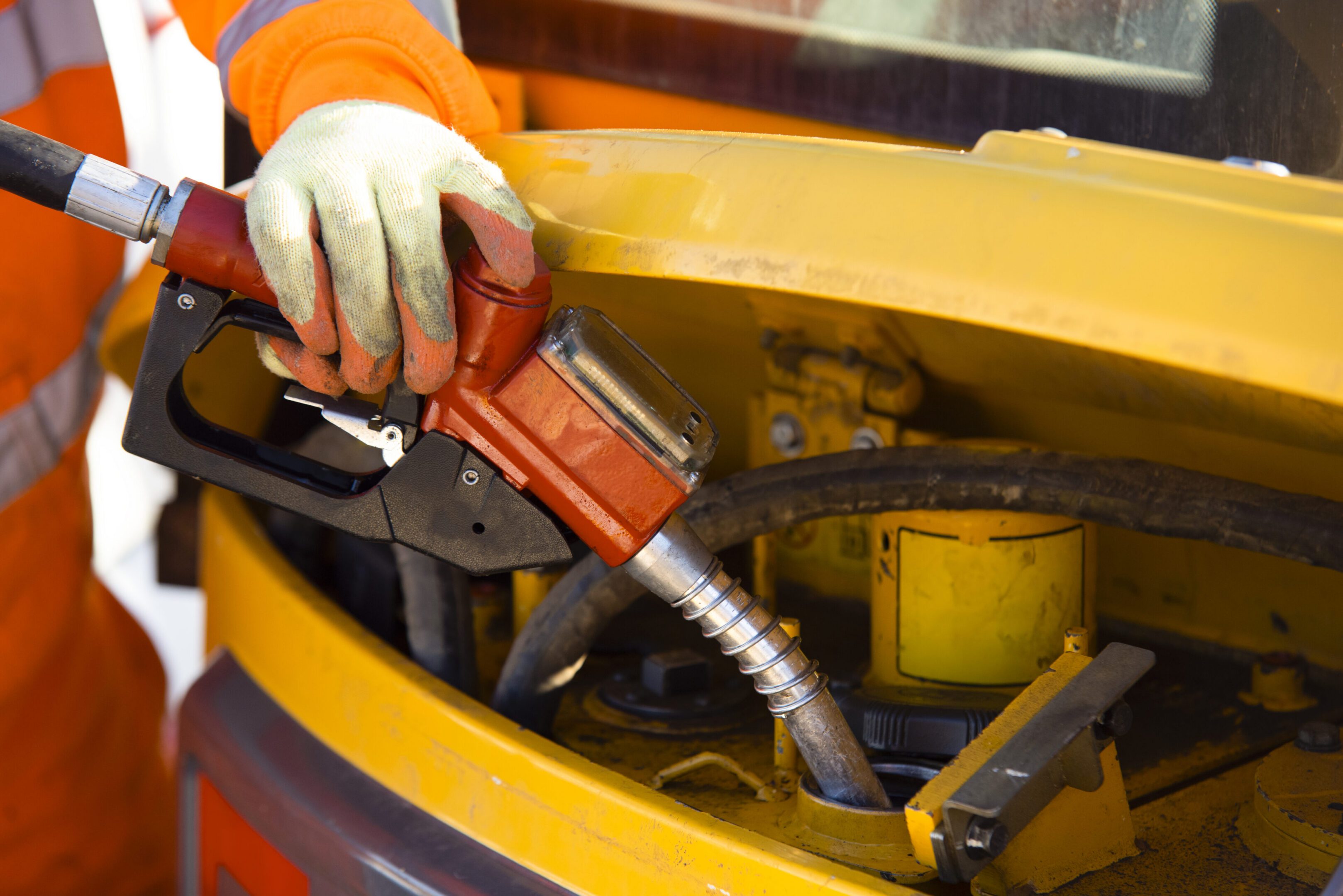 Gloved worker refueling yellow construction vehicle