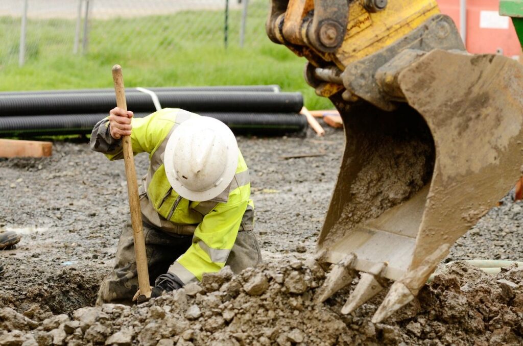 Construction worker digging by excavator bucket